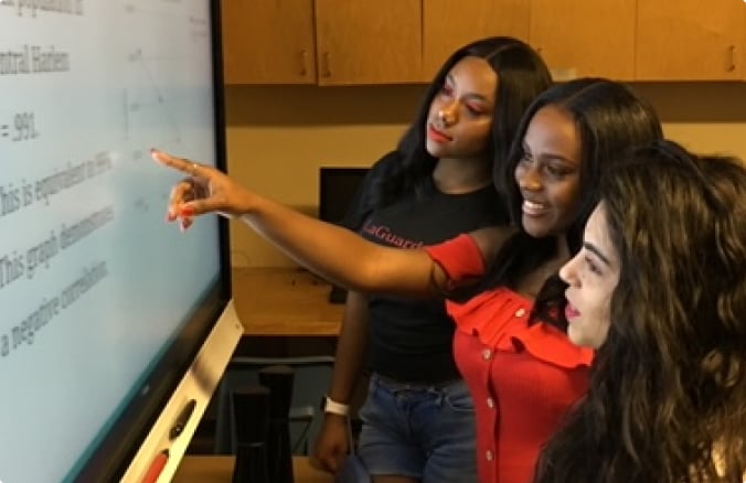 three girls pointing at smart board